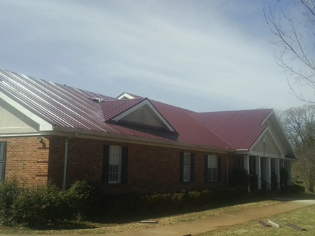 Red metal roof with gabled entries on a long brick building, from a Hail Damage Roof Repair job in Zanesville