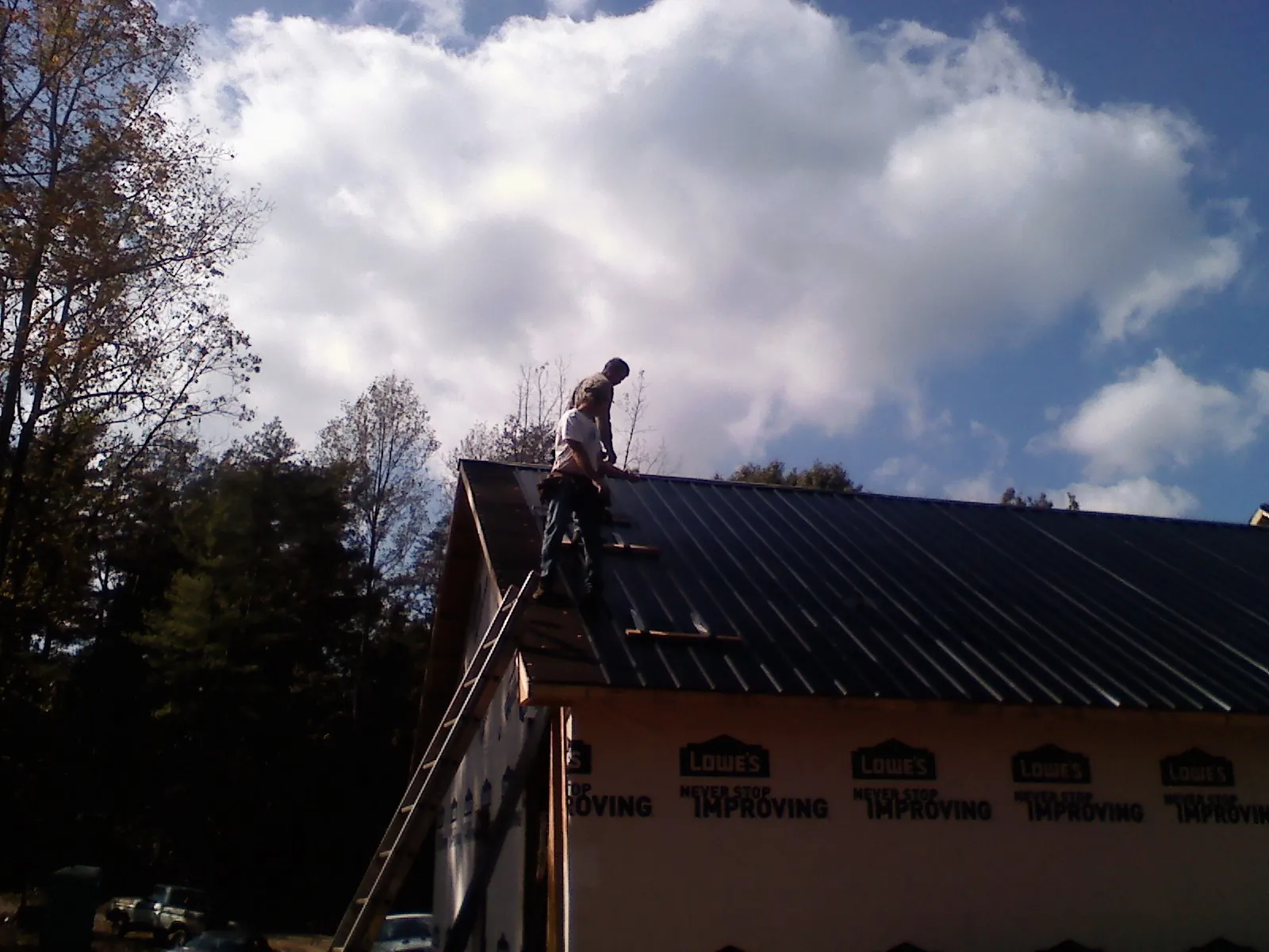 Roofer fastening dark metal panels high against a cloudy sky, from a Roof Inspection job in Zanesville
